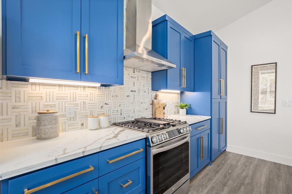 1606 Harvey Street, Unit 2 Austin, TX 78702 - Photo 6 of 22 Kitchen featuring blue shaker-style cabinetry with gold-finish hardware, stainless steel gas range with coordinating ventilation hood, white marble-look countertops, and a patterned tile backsplash