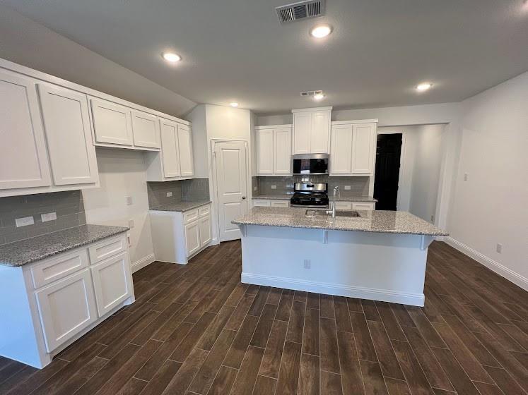 1408 Rendyn Street Anna, TX 75409 - Photo 5 of 23 Open-concept kitchen featuring white cabinetry, light-toned countertops, a central island with an integrated sink, modern stainless steel appliances, and wood-finish flooring