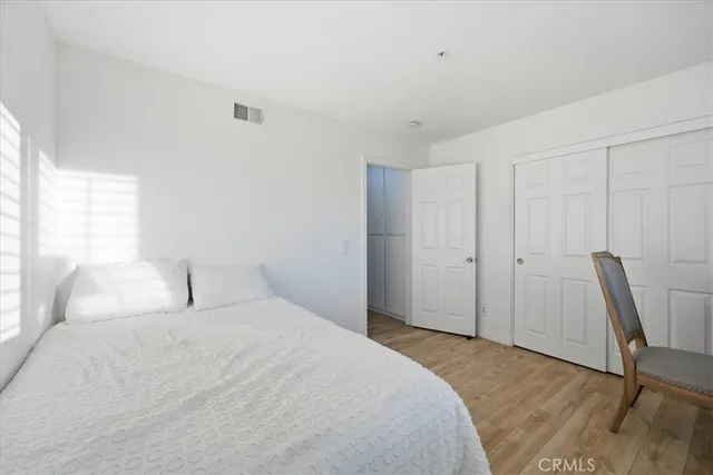 a bedroom with a bed a chair a potted plant on the dresser and a large window