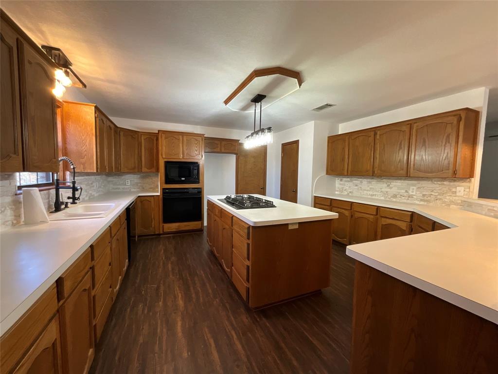999 West Boynton Street Hamilton, TX 76531 - Photo 21 of 26 a large kitchen with stainless steel appliances kitchen island granite countertop a stove a sink dishwasher and a refrigerator with wooden floor