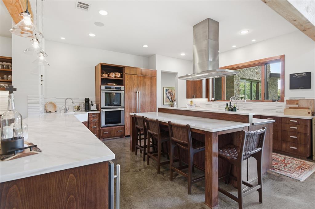 1138 Bancroft Road Keller, TX 76248 - Photo 12 of 39 Spacious kitchen featuring a large central island with seating, a professional-grade stainless steel range hood, integrated double ovens, warm wood-finish cabinetry, and white countertops