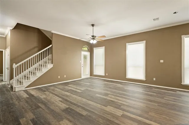 an empty room with wooden floor fan and windows