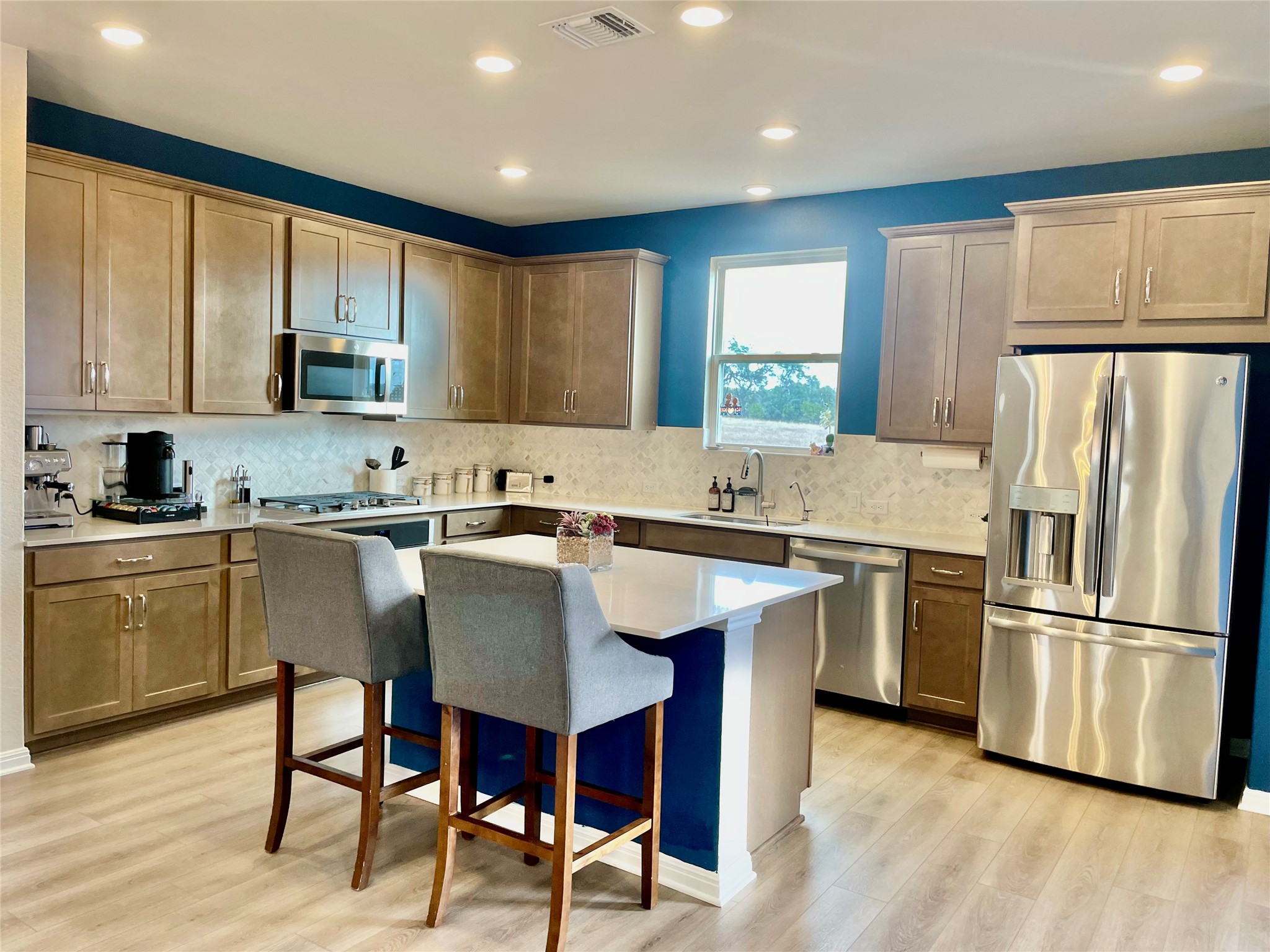 232 Denali Way Dripping Springs, TX 78620 - Photo 2 of 33 Kitchen with stainless steel appliances, a breakfast bar area, light wood-style floors, a kitchen island, and light stone counters