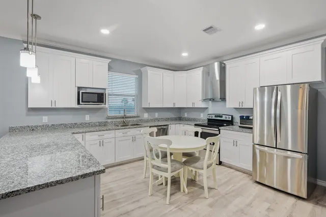 a kitchen with granite countertop stainless steel appliances a refrigerator a stove top oven a sink and white cabinets