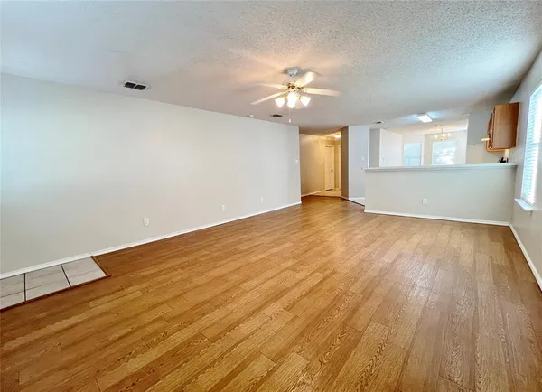 an empty room with wooden floor chandelier fan and windows