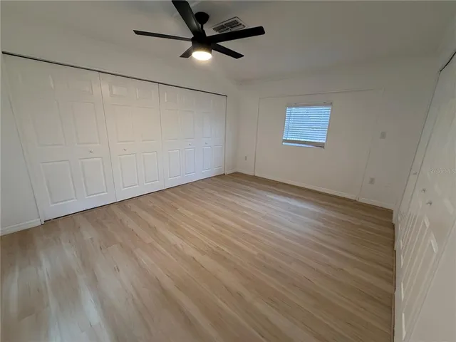 an empty room with wooden floor fan and windows