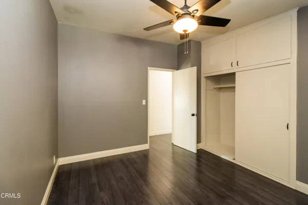 a view of an empty room with wooden floor and a ceiling fan