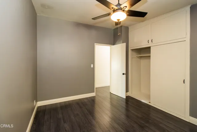 a view of an empty room with wooden floor and a ceiling fan