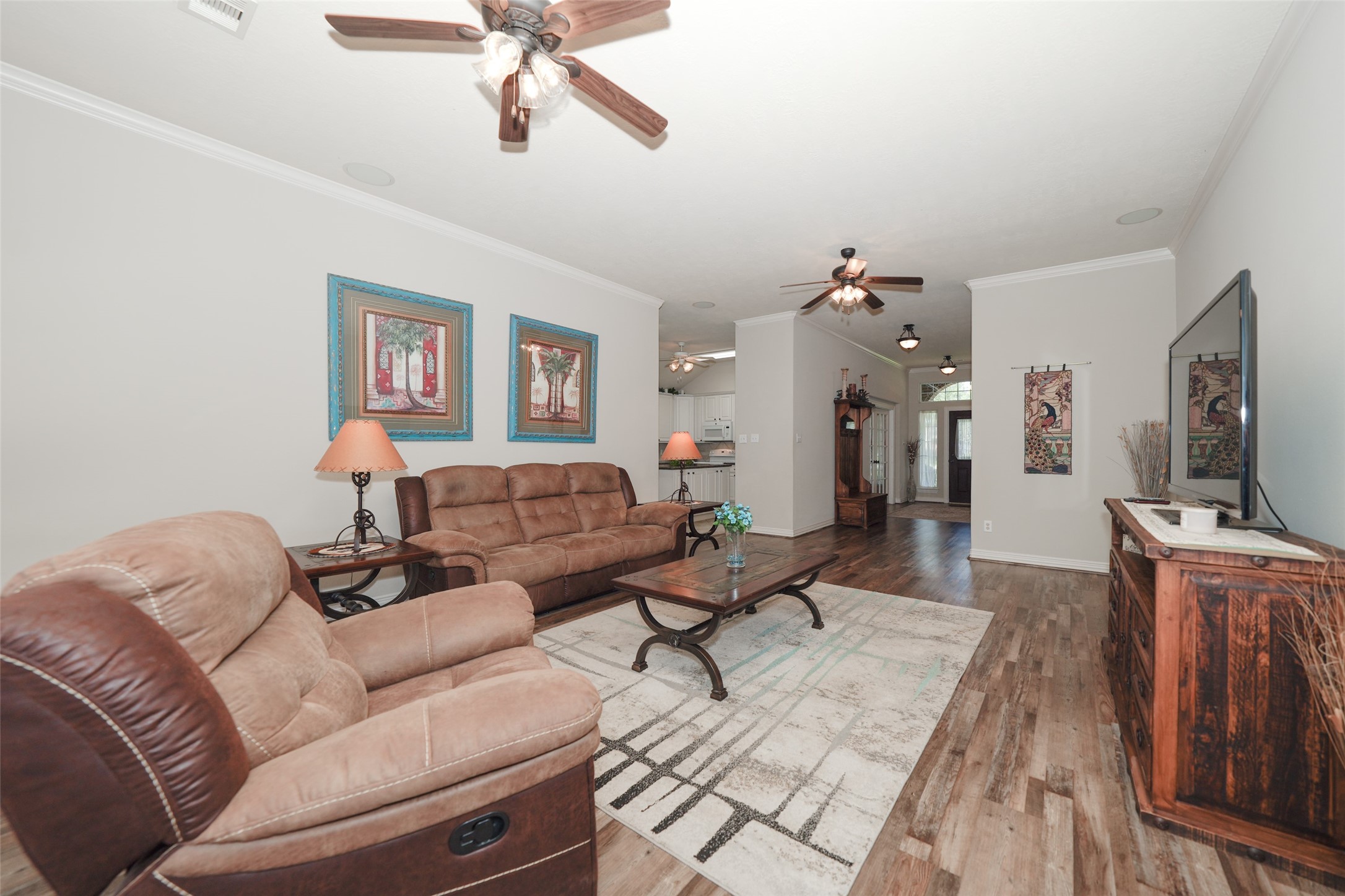 2203 Red Bird Lane Pattison, TX 77423 - Photo 17 of 46 This spacious living room features warm wood flooring, neutral walls, and ceiling fans for comfort. It includes cozy seating, a large TV, and decorative accents, creating a welcoming space for relaxation and entertainment. The room is open to the kitchen, enhancing the flow and functionality of the home.