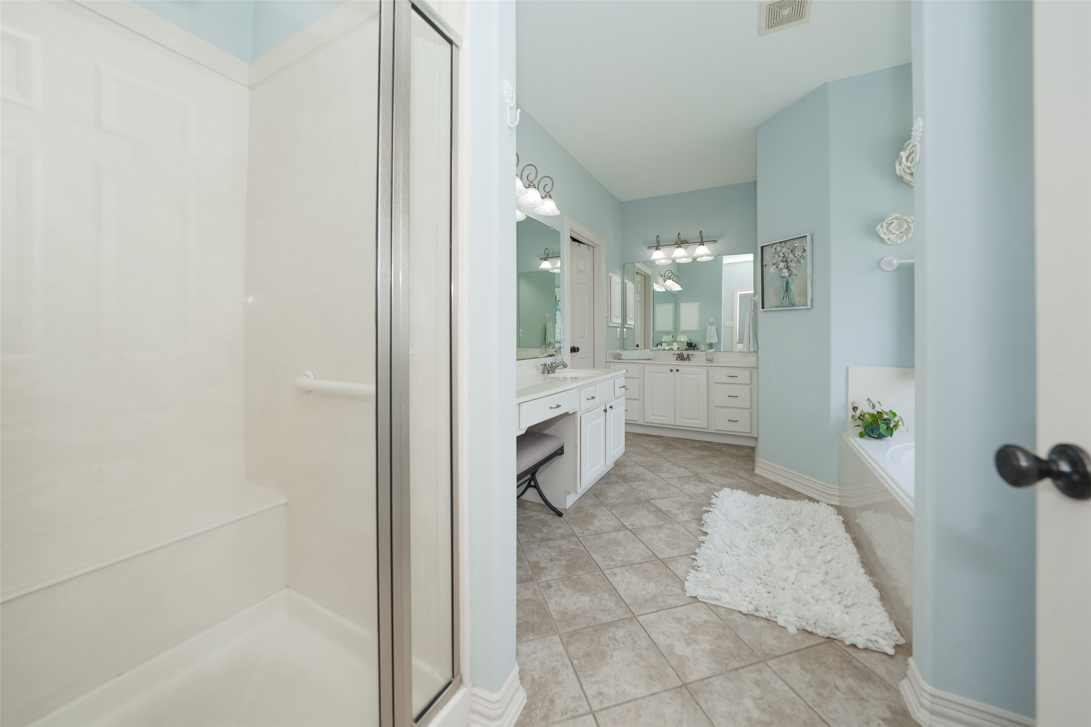2203 Red Bird Lane Pattison, TX 77423 - Photo 25 of 46 This bathroom features a spacious layout with a large walk-in shower, a double vanity with ample storage, and a separate bathtub. The light blue walls and tiled floor create a serene atmosphere, complemented by modern lighting and fixtures.