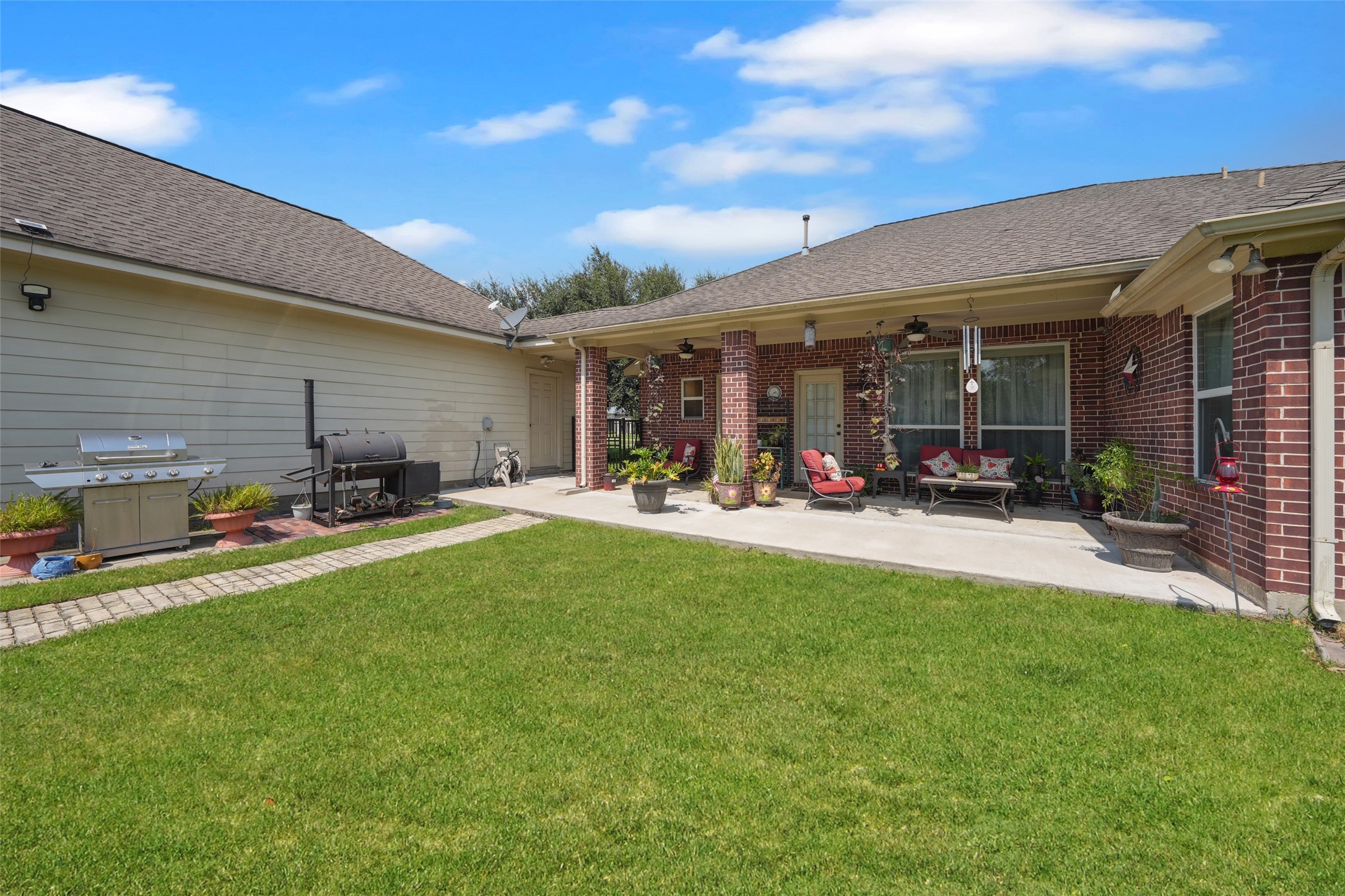 2203 Red Bird Lane Pattison, TX 77423 - Photo 31 of 46 This photo showcases a spacious backyard with a well-maintained lawn and a cozy covered patio. The patio features comfortable seating, decorative plants, and is perfect for outdoor entertainment. There's also a barbecue area, ideal for hosting gatherings.