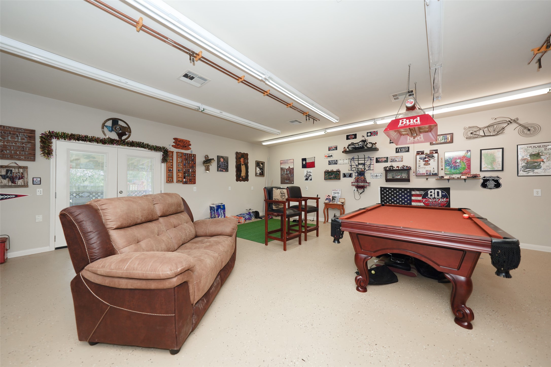 2203 Red Bird Lane Pattison, TX 77423 - Photo 34 of 46 This spacious game room features a pool table, comfortable seating, and wall decor with a sports and automotive theme. It includes ample lighting and double doors leading outside, creating an inviting recreational space.