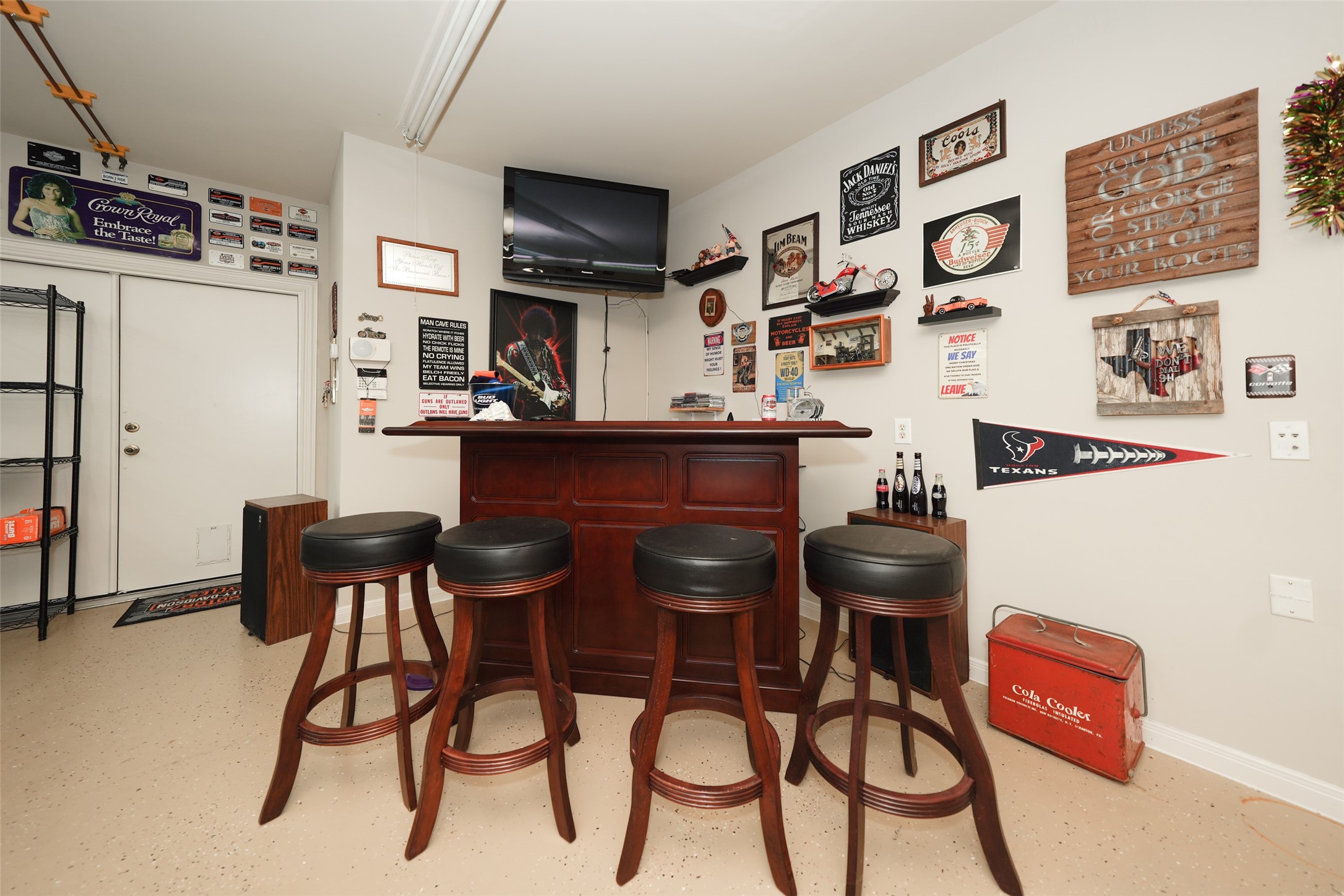 2203 Red Bird Lane Pattison, TX 77423 - Photo 35 of 46 This photo shows a cozy home bar area with a wooden bar counter and four bar stools. The walls are decorated with various signs and memorabilia, and there's a TV mounted above for entertainment. It's a perfect spot for relaxing or hosting guests.