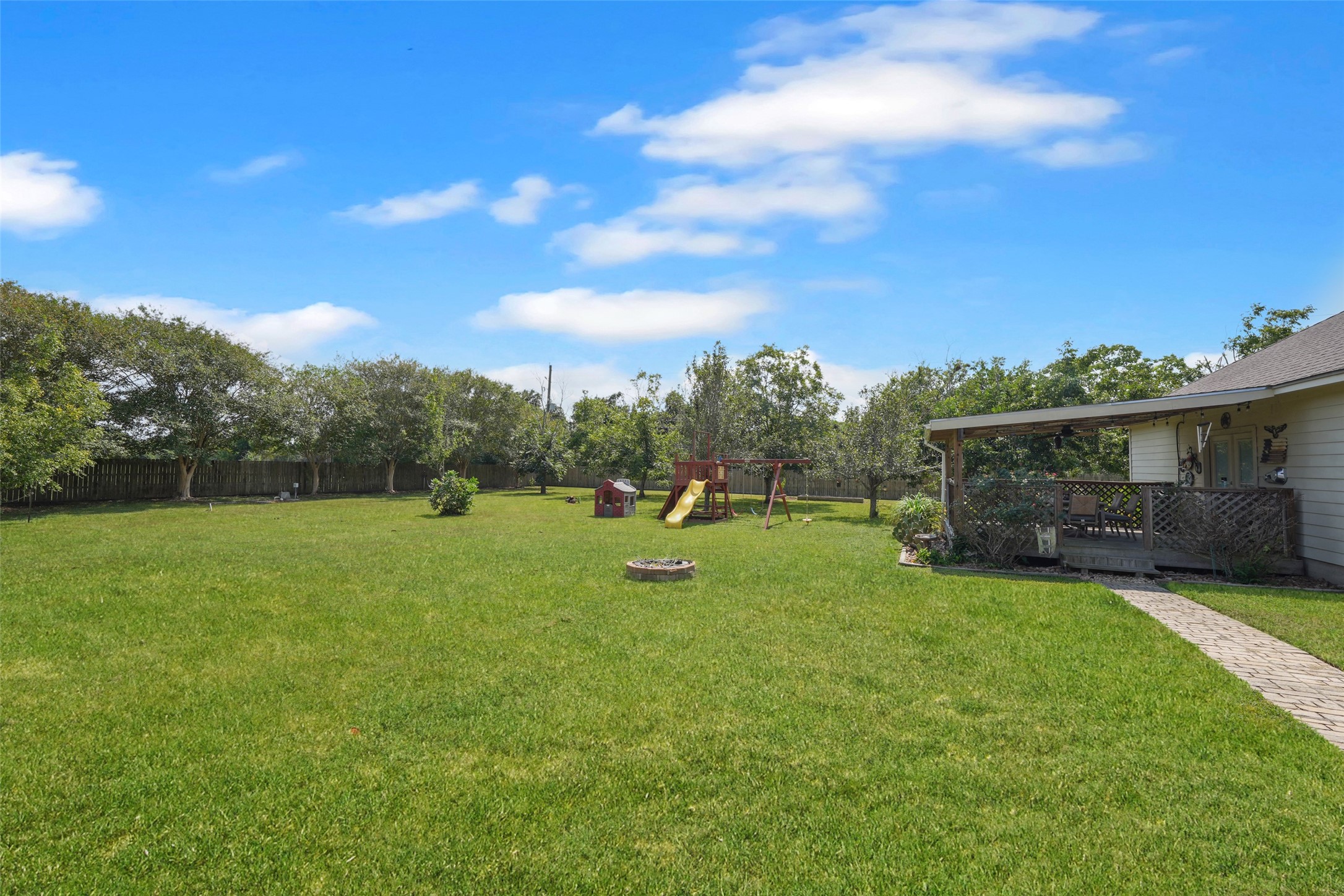 2203 Red Bird Lane Pattison, TX 77423 - Photo 42 of 46 Spacious backyard with lush green lawn, a playset for kids, and a cozy covered patio, perfect for family gatherings and outdoor activities.
