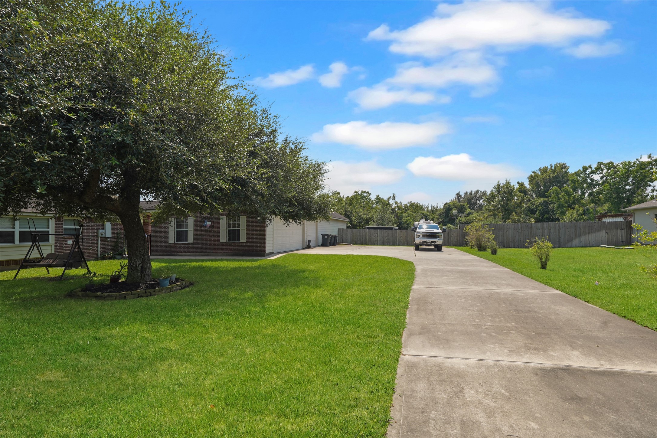 2203 Red Bird Lane Pattison, TX 77423 - Photo 45 of 46 This photo shows a charming home with a large, well-maintained lawn and a long driveway leading to a garage. The property is framed by mature trees, offering shade and privacy, with a fenced backyard that adds security.