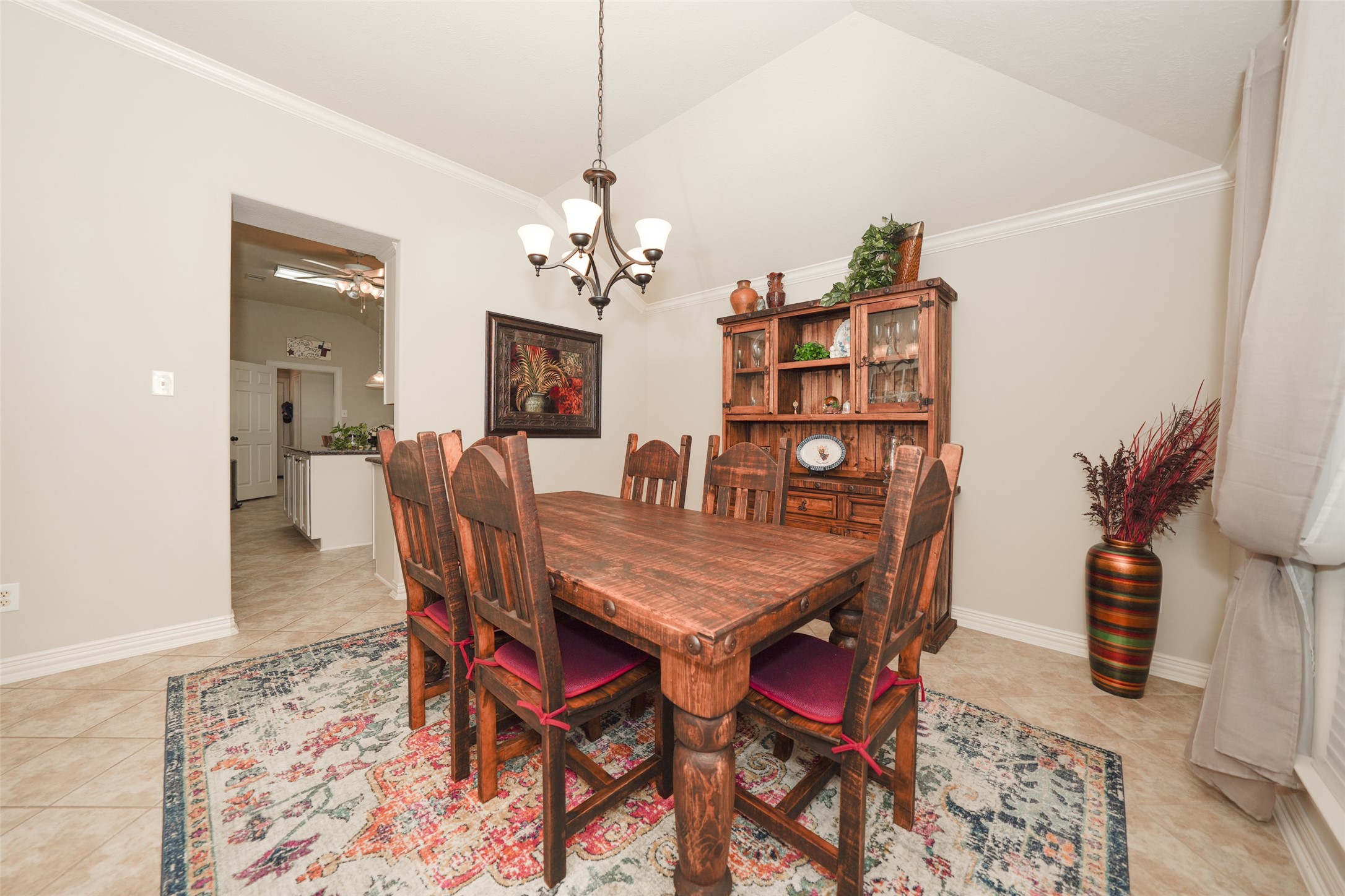 2203 Red Bird Lane Pattison, TX 77423 - Photo 8 of 46 This dining room features a rustic wooden table with matching chairs, set on a patterned rug. A wooden hutch provides storage and decoration. The room has neutral walls, tiled flooring, and a chandelier, creating a cozy and inviting atmosphere.