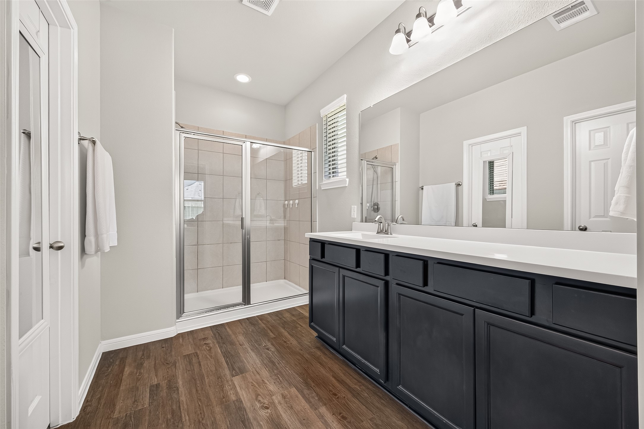1329 Red Hills Drive Rosharon, TX 77583 - Photo 17 of 27 This bathroom features a modern design with a spacious glass-enclosed shower, sleek dark cabinetry, and a large mirror above the sink. The flooring adds a warm touch, while neutral walls and ample lighting create a bright, inviting space.