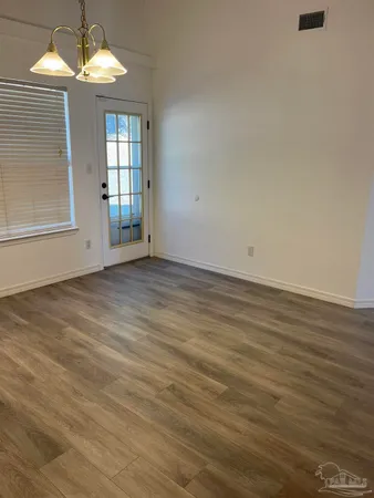 an empty room with wooden floor chandelier and windows