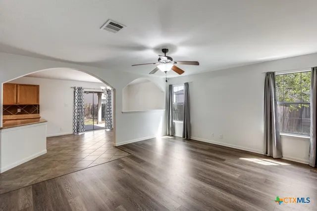 a view of a livingroom with wooden floor a ceiling fan and windows
