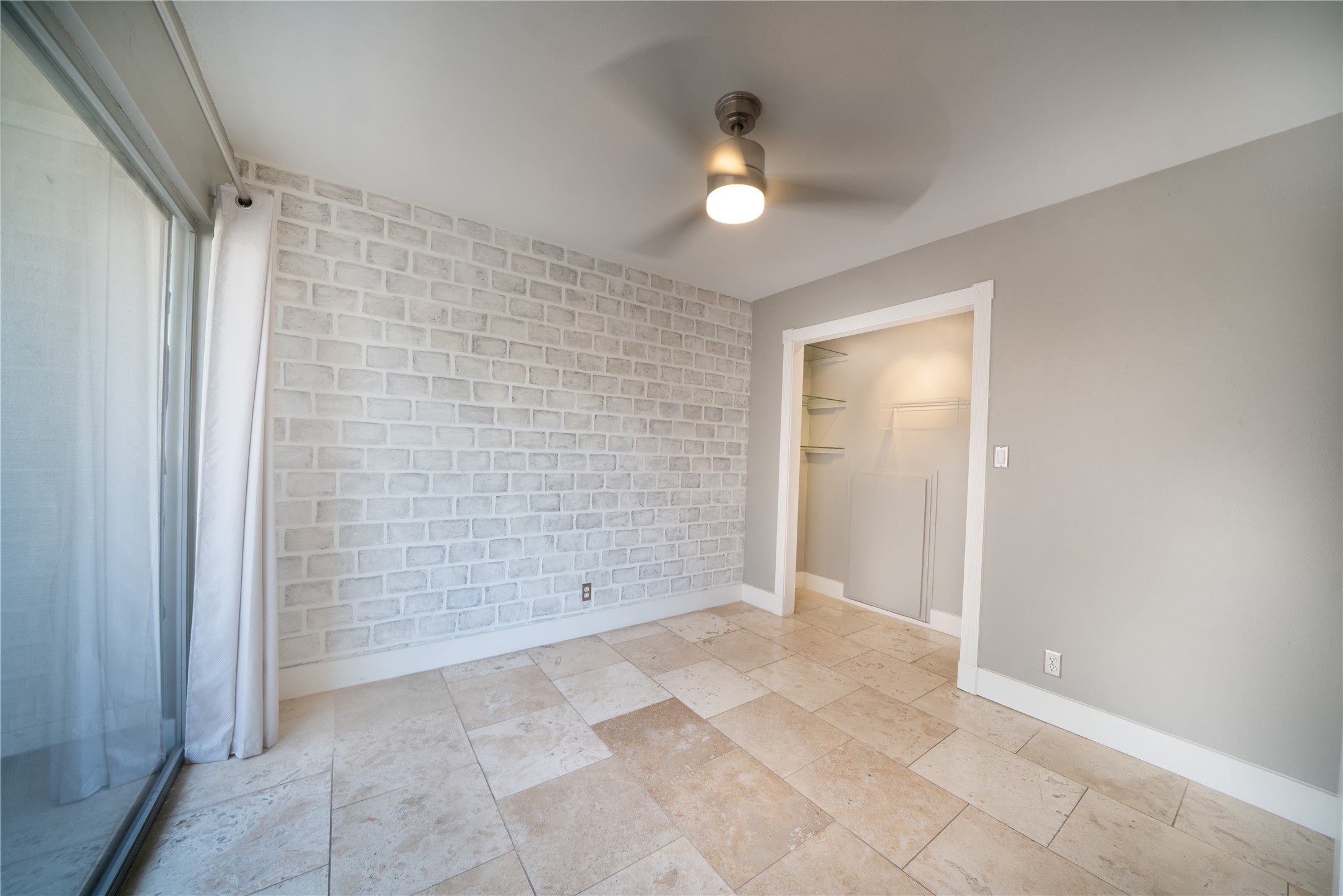 500 East Riverside Drive, Unit 242 Austin, TX 78704 - Photo 13 of 40 Unfurnished bedroom featuring stone tile floors, a closet, brick wall, baseboards, and ceiling fan