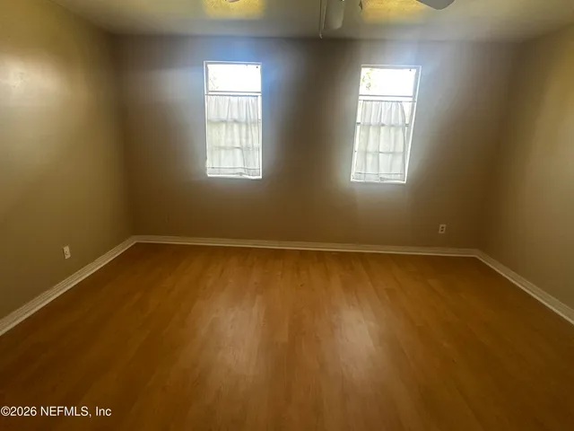an empty room with wooden floor and windows with curtains