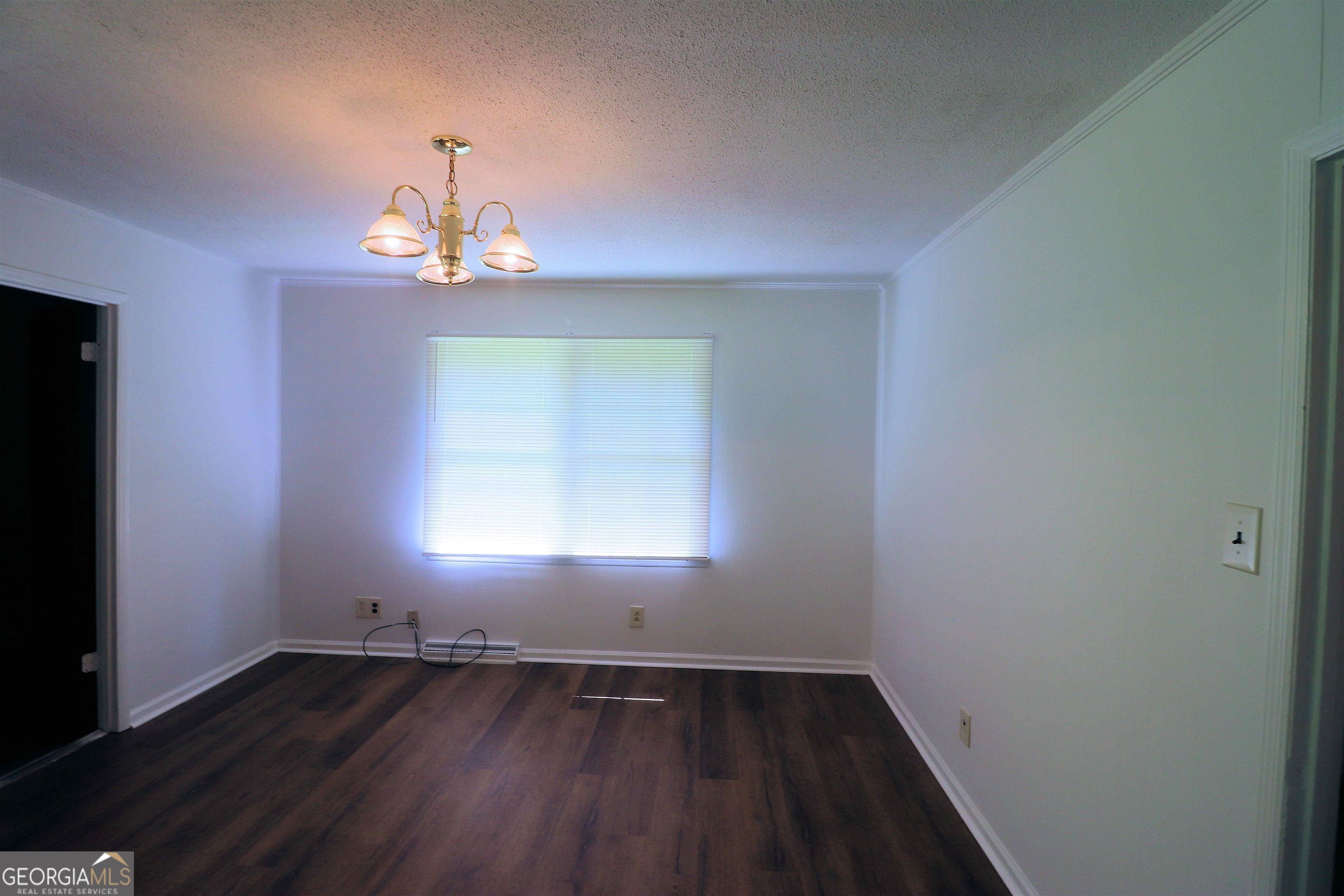 156 Deacon J Simmons Road Southwest Milledgeville, GA 31061 - Photo 4 of 12 an empty room with wooden floor chandelier and windows