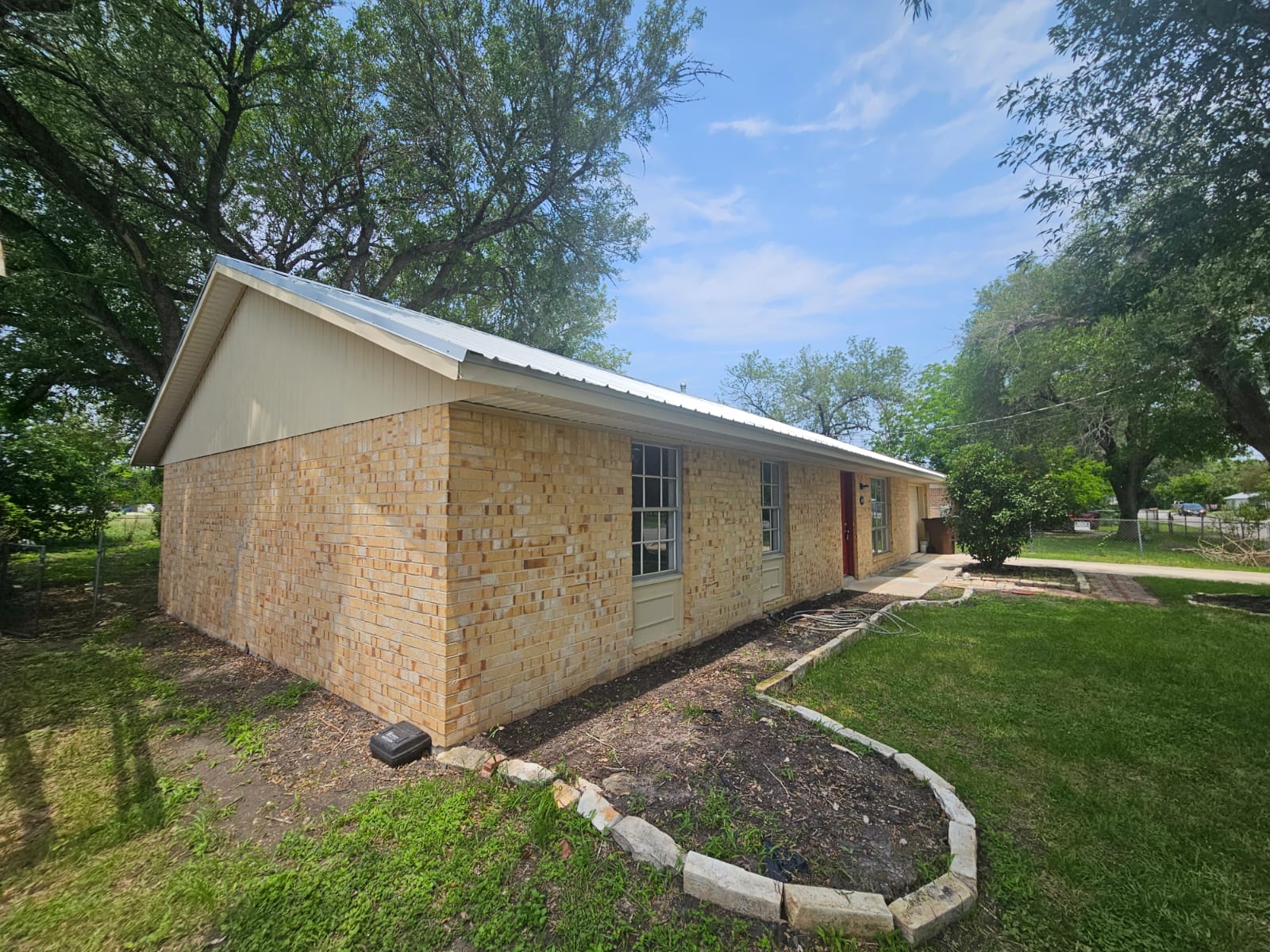 1401 Trinity Street Lockhart, TX 78644 - Photo 25 of 31 Exterior features light-colored brick siding, a light-colored metal roof, and white soffit and fascia