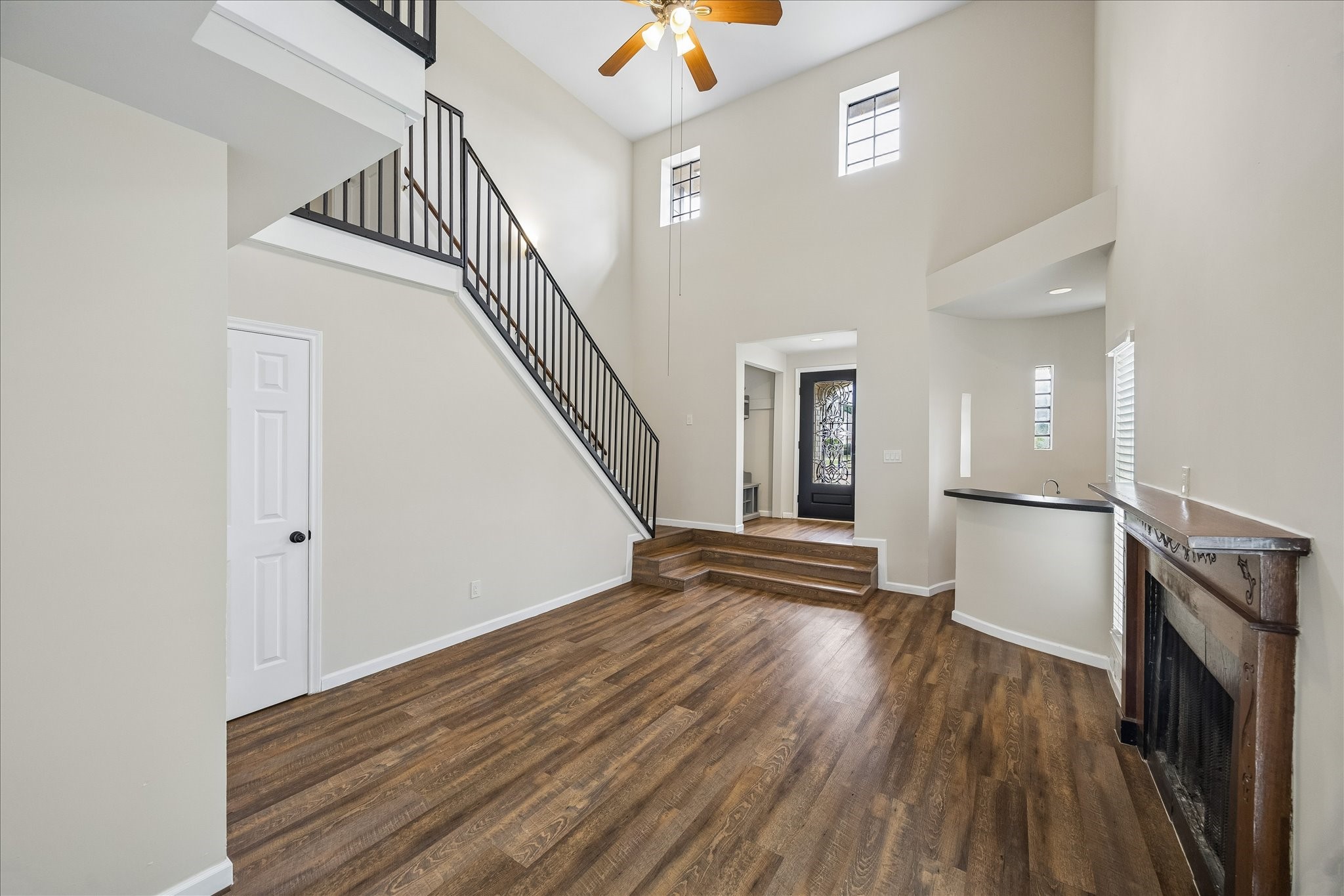 10411 Goodrum Road Houston, TX 77041 - Photo 6 of 25 Dramatic two-story family room featuring soaring ceilings, wood-look flooring, a cozy fireplace, and an elegant staircase with iron railings. The open layout and abundant natural light create a spacious, inviting setting ideal for everyday living and entertaining.