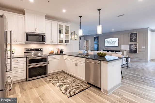 a kitchen with stainless steel appliances granite countertop a stove top oven a sink dishwasher a refrigerator and a dining table with wooden floor