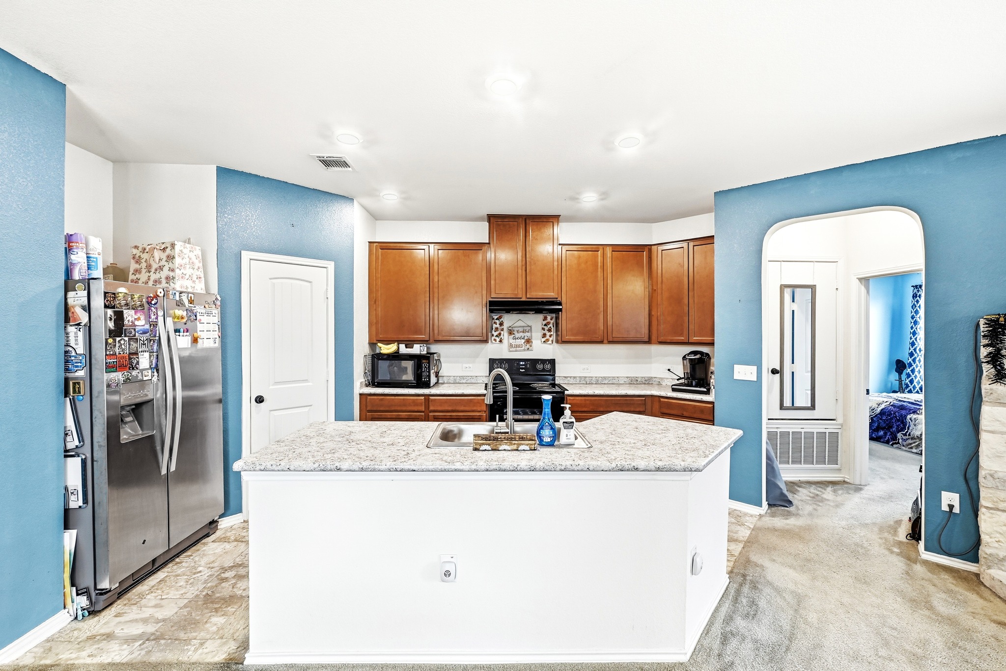 1621 Dragonfly Loop Bastrop, TX 78602 - Photo 12 of 27 Kitchen featuring a central island with a sink, wood cabinetry, light-toned countertops, and recessed lighting