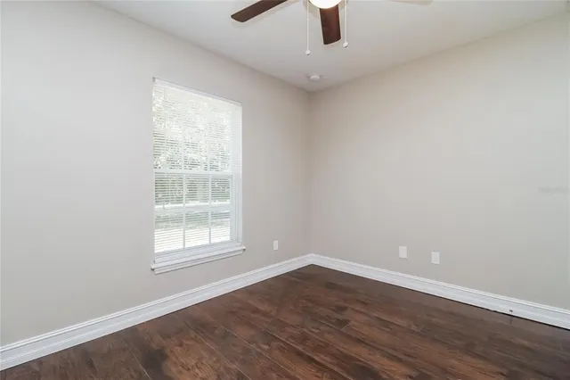 an empty room with wooden floor fan and windows