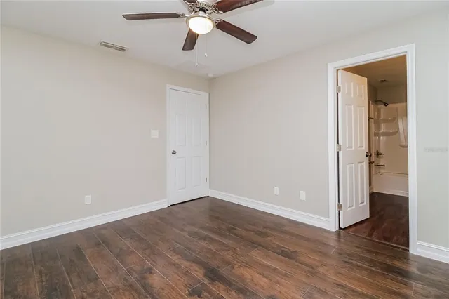 an empty room with wooden floor fan and windows