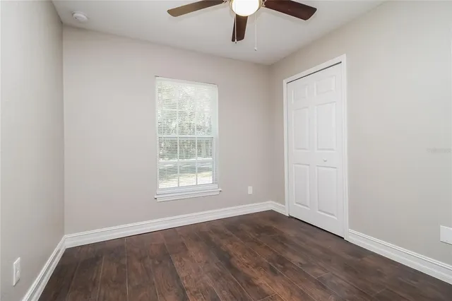 an empty room with wooden floor chandelier fan and windows