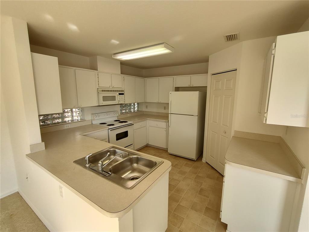 7257 Southwest 115th Place Ocala, FL 34476 - Photo 7 of 18 a kitchen with refrigerator a stove a microwave and white cabinets