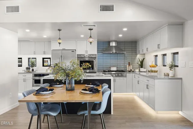 a kitchen with stainless steel appliances kitchen island granite countertop a dining table chairs and white cabinets