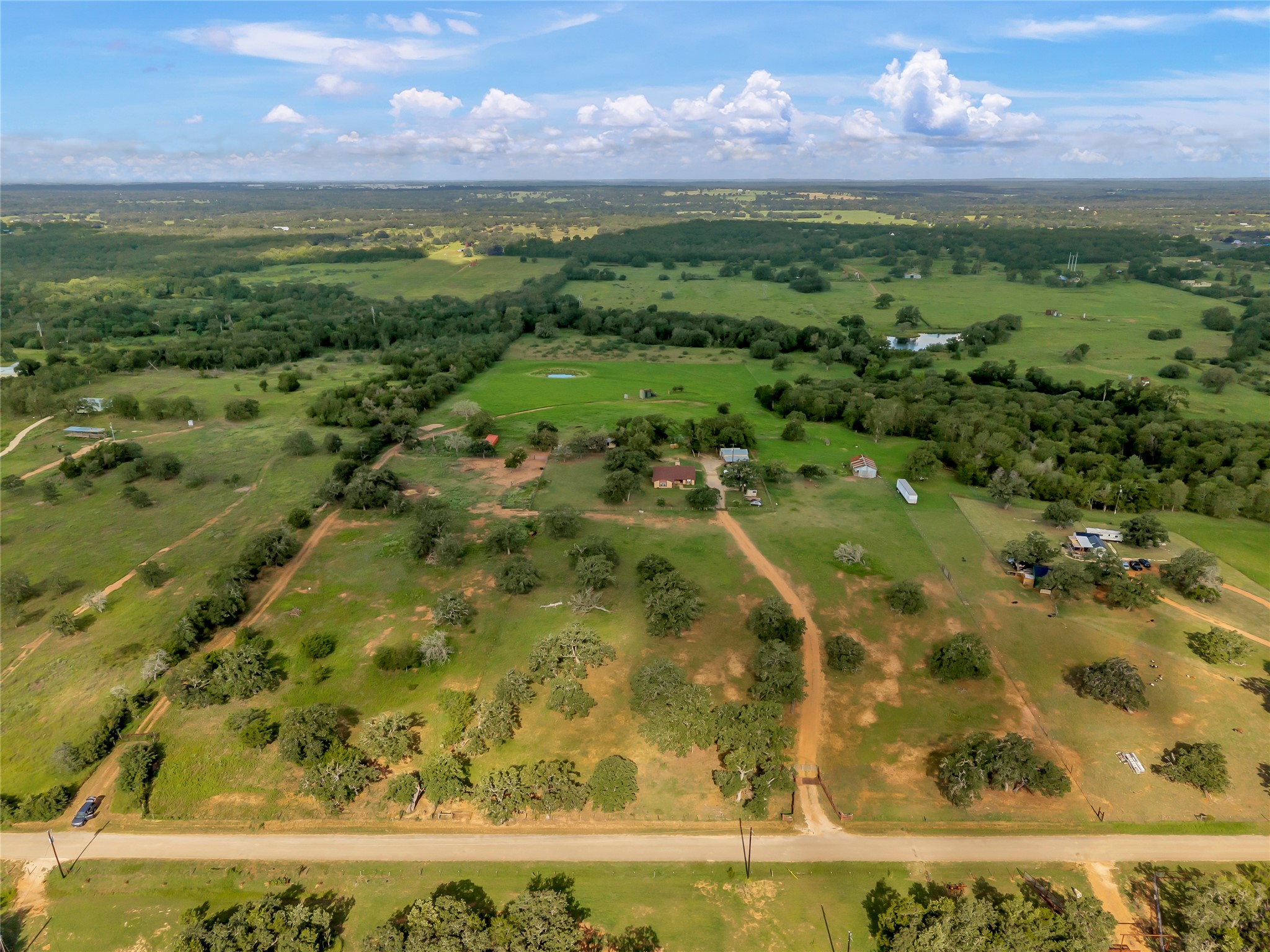 A vast expanse of green pastureland features mature trees under a wide, blue sky.
