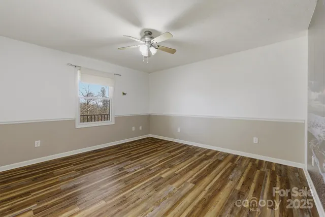a view of an empty room with wooden floor and a fan