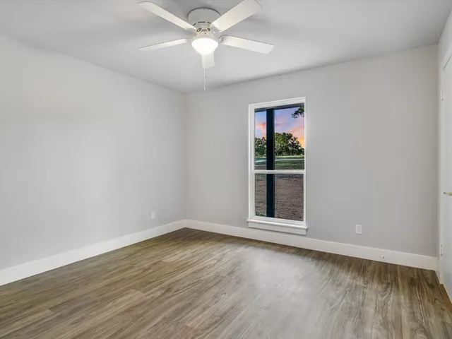 an empty room with wooden floor chandelier fan and windows