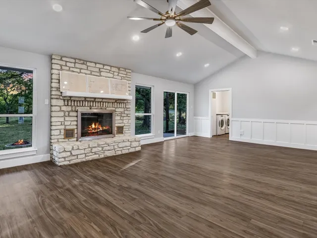 an empty room with wooden floor fireplace cabinet and windows