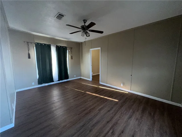 an empty room with wooden floor a ceiling fan and windows