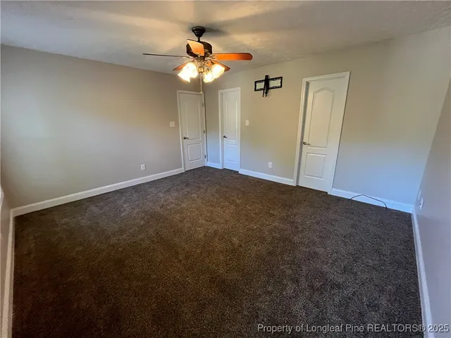 an empty room with a chandelier fan and wooden floor