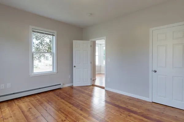 a view of an empty room with wooden floor and a window