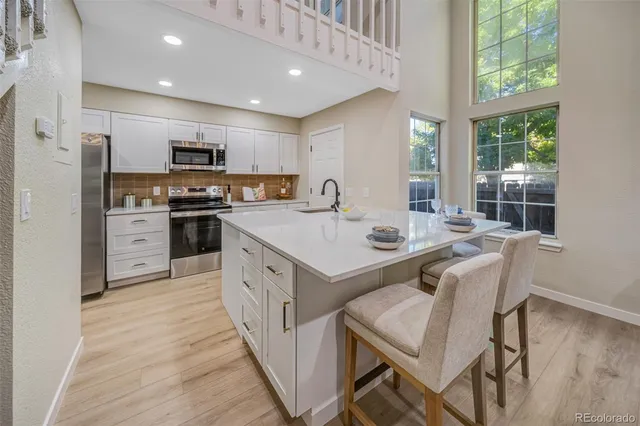 a large kitchen with stainless steel appliances granite countertop a stove a sink a microwave a refrigerator and white cabinets with wooden floor
