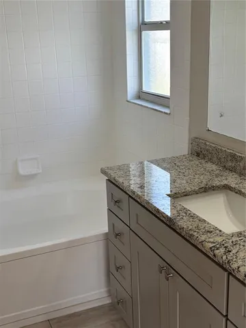 a bathroom with a granite countertop bathtub shower sink vanity and toilet