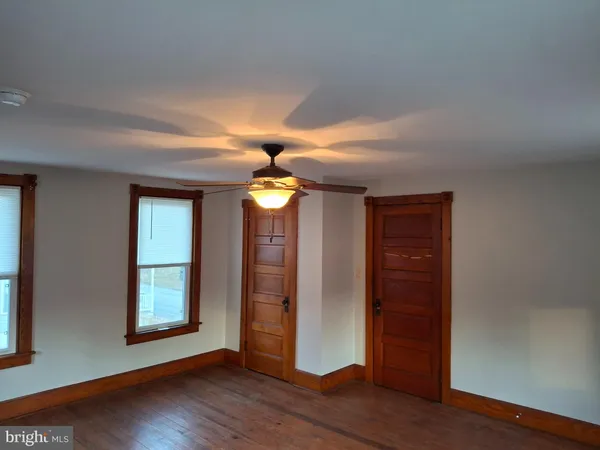 an empty room with wooden floor chandelier fan and windows