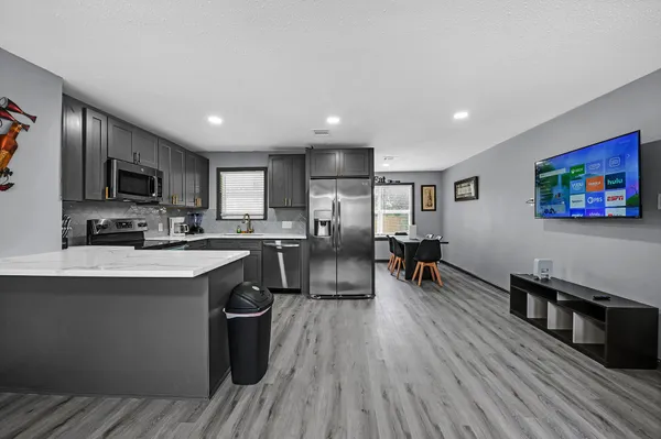 a kitchen with stainless steel appliances granite countertop a refrigerator oven a sink dishwasher a dining table and chairs with wooden floor