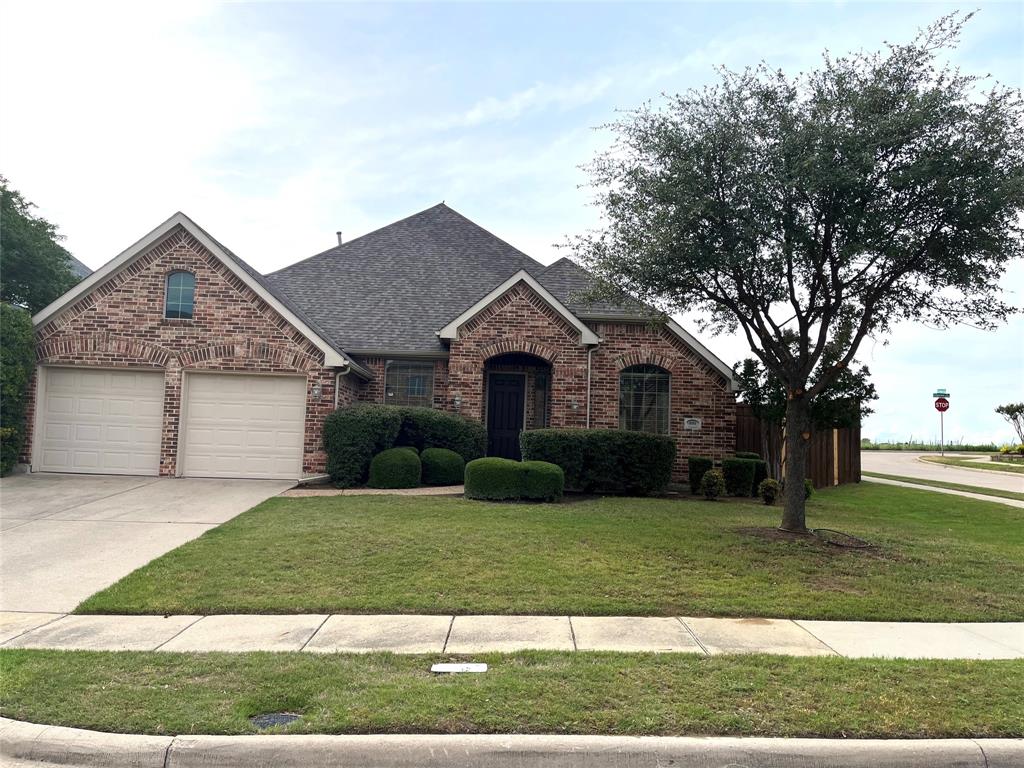 Brick exterior featuring a two-car garage, arched entryways, a gabled roofline, mature landscaping, and a manicured lawn