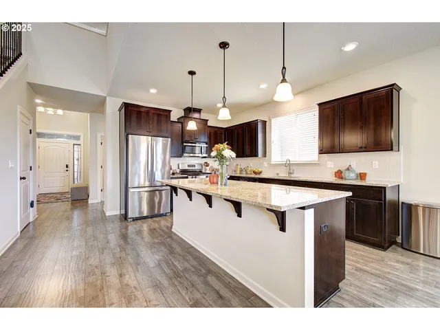 a open kitchen with stainless steel appliances granite countertop a stove top oven a sink dishwasher a dining table and chairs with wooden floor