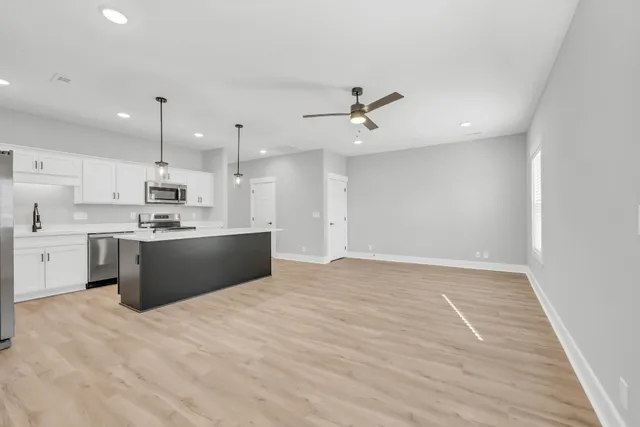 a large white kitchen with kitchen island a sink dishwasher a stove a refrigerator and white cabinets with wooden floor