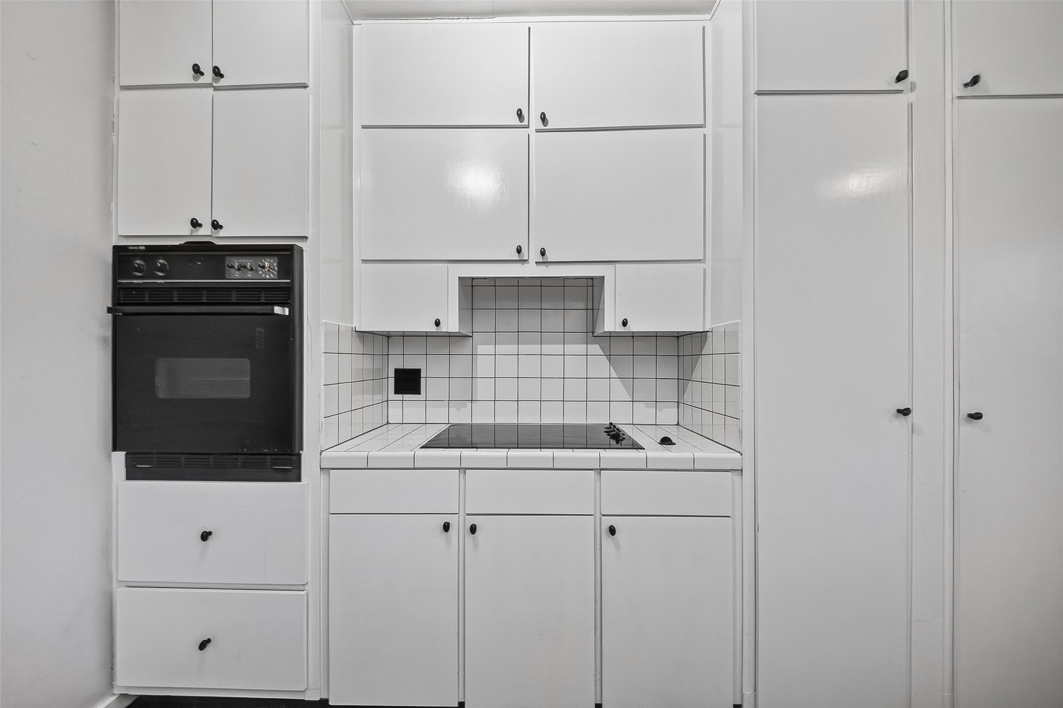 1758 Hawthorne Street, Unit 2 Houston, TX 77098 - Photo 11 of 19 This kitchen features modern appliances with a built-in oven and microwave, ample white cabinetry for storage, and a stylish tiled backsplash. The space is bright, with a window and door leading outside, complemented by sleek countertops and tiled flooring.